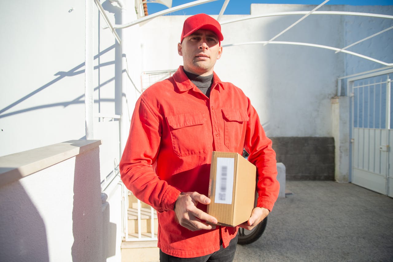 A male delivery worker in a red uniform holding a package outdoors in Portugal.