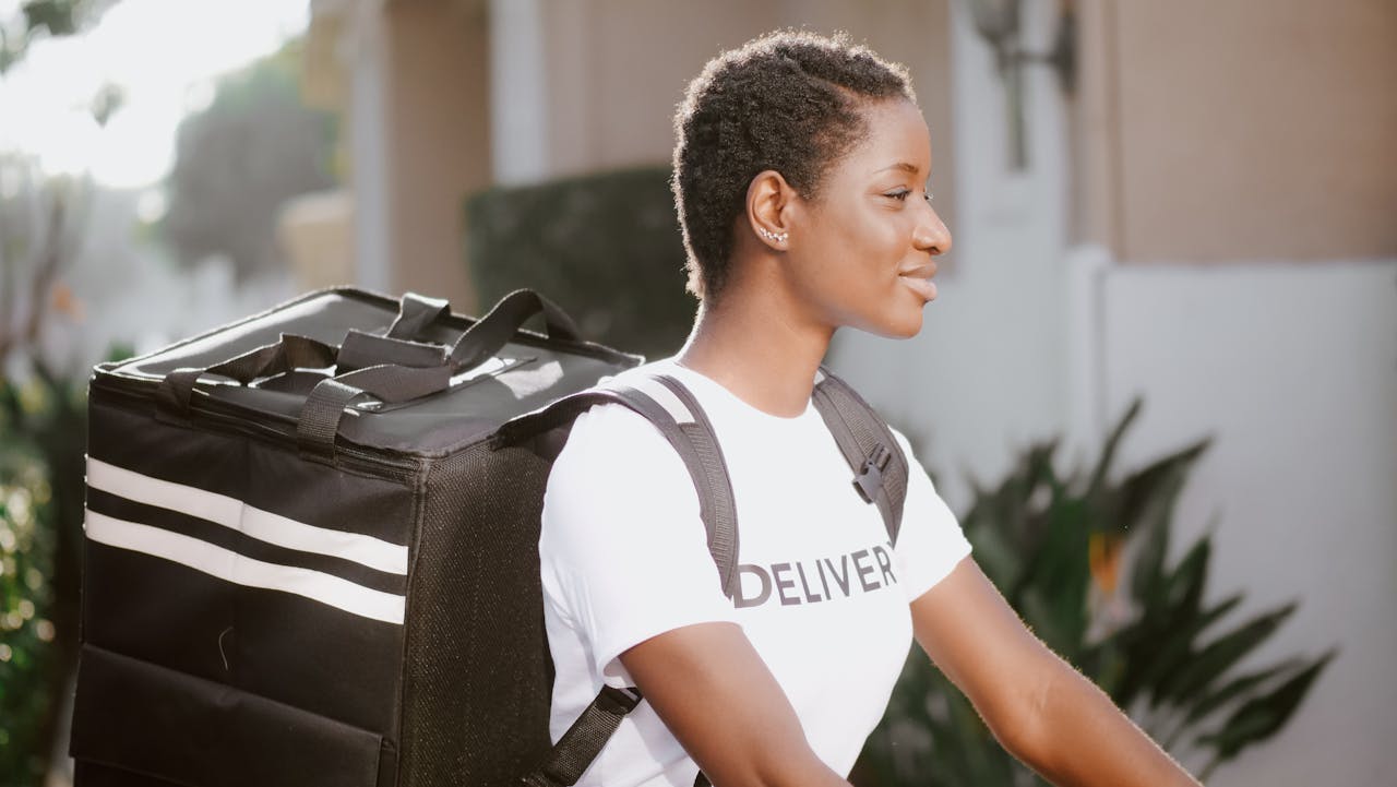 Smiling female delivery person with backpack outdoors during the day.